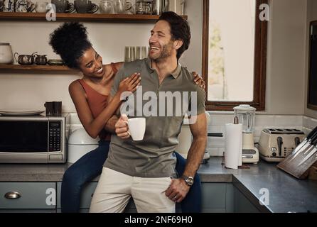 Du bist so witzig, weißt du das? Ein liebevolles junges Paar, das zusammen lacht, während es Zeit in der Küche zu Hause verbringt. Stockfoto