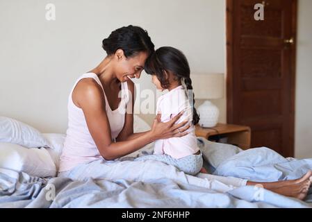 Nichts kommt dir in dieser Welt nahe. Eine wunderschöne junge Mutter, die sich mit ihrem kleinen Mädchen im Bett zu Hause anfreundet. Stockfoto