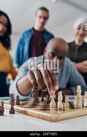 Beschütze den König um jeden Preis. Ein erwachsener Geschäftsmann, der in seinem Büro Schach spielt, während seine Kollegen im Hintergrund zuschauen. Stockfoto