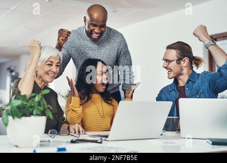 Unsere harte Arbeit zahlt sich aus. Eine Gruppe fröhlicher Geschäftsleute, die gemeinsam einen Laptop-Bildschirm betrachten und im Büro voller Spannung jubeln. Stockfoto
