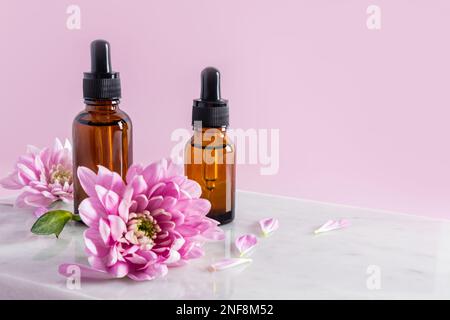 Zwei Kosmetikflaschen mit einer Pipette mit ultrafeuchtigkeitsspendendem Serum für das Gesicht stehen auf weißen Marmorfliesen zwischen den Blumen. Rosafarbener Hintergrund Stockfoto