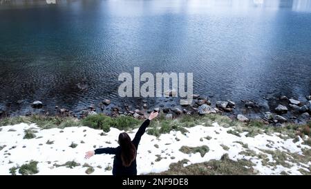 Glückliche Frau, die die Czarny Staw pod Rysamy oder den Black Pond See in der Nähe der Morskie Oko Snowy Mountain Hut in den polnischen Tatry Bergen genießt, Blick auf die Drohne, Zakopane, Polen. Einheit mit Natur Luftaufnahme der wunderschönen grünen Hügel und Berge in dunklen Wolken und Reflexion auf dem See Morskie Oko. Reiseziel 4K Stockfoto