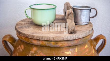 Großer Becher aus Steingut mit Deckel und Trinkwasserbecher. Altes Cottage Küchenkonzept Stockfoto