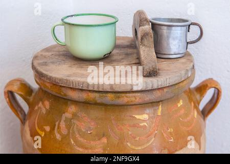 Großer Becher aus Steingut mit Deckel und Trinkwasserbecher. Altes Cottage Küchenkonzept Stockfoto