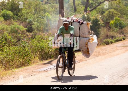 Befato, Madagaskar - 11. November. 2022: Ein madagassischer Mann auf einem Fahrrad transportiert große Säcke. Traditioneller Transport der armen Bevölkerung in Madagaskar Stockfoto