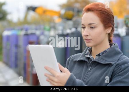 Arbeiterin, die ein digitales Tablet im Hof mit Gaskanistern benutzt Stockfoto