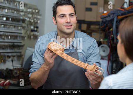 Männliche Mitarbeiterin, die weibliche Kundin bei der Auswahl des Gürtels unterstützt Stockfoto