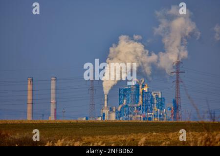 Industrielle Szene mit Schornstein, Silos, Holzhaufen und Rauch am stürmischen Himmel. Holzindustrie. Möbelfabrik. Stockfoto