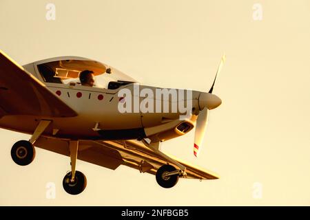 Kleines Propellerflugzeug, das am Nachmittag unter der Dämmerung auf der Landebahn des Flughafens Sabadell mit einem völlig orangefarbenen blauen Himmel landet oder abhebt. Stockfoto