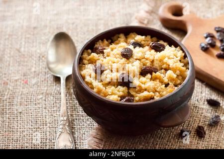 Süßer Hirseporridge mit dunklen Rosinen in einer rustikalen Keramikschale Stockfoto