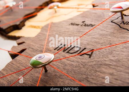 Indische Flagge auf der Drucknadel und rote Fäden auf der hölzernen Karte. Reise- oder Logistikrouten. Einfluss in Geopolitik und Weltwirtschaft. Stockfoto