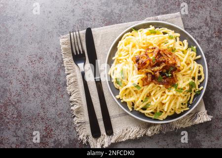 Eiernudeln mit geschmolzenem Käse und gebratenen Zwiebeln in der Nahaufnahme auf einem Teller auf dem Tisch. Horizontale Draufsicht von oben Stockfoto