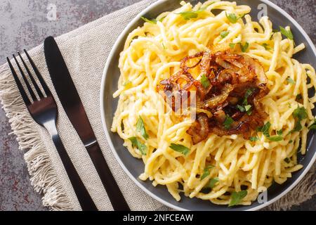 Heiße Nudeln und geriebener Käse Emmentaler, garniert mit gebratenen Zwiebeln auf dem Teller auf dem Tisch. Horizontale Draufsicht von oben Stockfoto