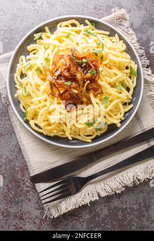 Tiroler Käse-Nudeln oder Pasta namens Kaespaetzle mit gebratener Zwiebel auf dem Teller auf dem Tisch. Vertikale Draufsicht von oben Stockfoto