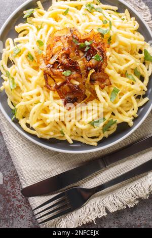 Traditionelles Kasespatzle-Käse-Splitzergericht serviert mit gebratenen Zwiebeln auf dem Teller auf dem Tisch. Vertikale Draufsicht von oben Stockfoto