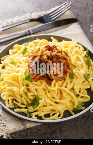 Kasespatzle deutscher Käse Spaetzle mit gebratenen Zwiebeln auf dem Teller auf dem Tisch. Vertikal Stockfoto