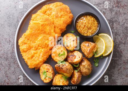 Köstliches deutsches Münchner Schnitzel, paniert mit Senf und Meerrettich, serviert mit gebackenen Kartoffeln aus nächster Nähe auf einem Teller auf dem Tisch. Horizontal t Stockfoto