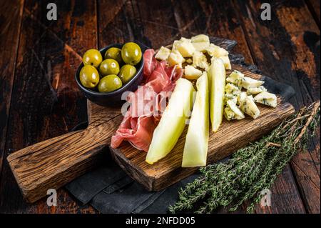 Käse- und Fleischplatte, Antipasti mit Prosciutto-Schinken, Parmesan, Blauschimmelkäse, Melone und Oliven auf Holzbrett. Holzhintergrund. Draufsicht. Stockfoto