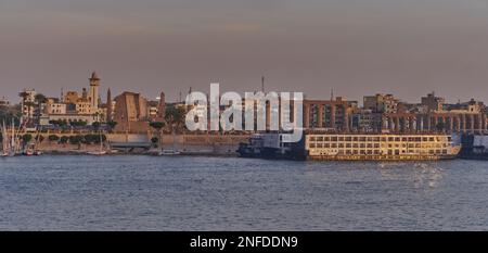 Luxor, ägyptischer Sonnenuntergang vom Westufer aus, der den Nil mit Felukken, Kreuzfahrtschiffen und dem Luxor Tempel am Ostufer zeigt Stockfoto