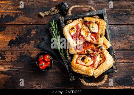 Blätterteig Tortenpizza mit Artischocke, Mozzarella, Tomaten und Käse in einem Holztablett. Holzhintergrund. Draufsicht. Stockfoto