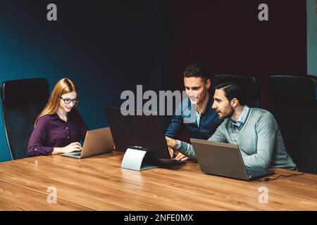 Geschäftsfrau und zwei ihrer Kollegen, die in einem dunklen Büro ohne Tageslicht arbeiten Stockfoto