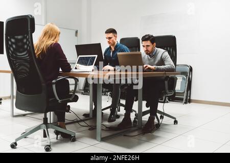 Eine Gruppe von drei jungen Geschäftsleuten, die in einem neu gegründeten Unternehmen arbeiten und im selben Büro arbeiten, jeder mit seinem eigenen Laptop Stockfoto