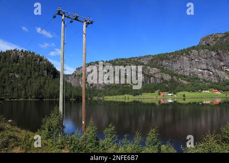 Das Dorf am See in Setesdal, Norwegen. Elektrischer Holzmast in der Region Agder. Stromleitungen des Stromnetzes. Stockfoto