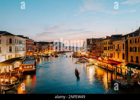 Venedig, Italien - 2022. Oktober: Blick auf Venedigs Canal Grande bei Sonnenuntergang mit beleuchteten Veranstaltungsorten am Ufer und Booten, die ihn überqueren Stockfoto