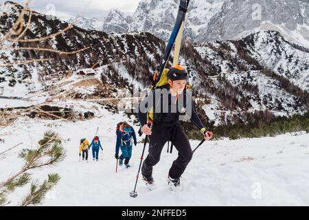 Eine Gruppe von Bergsteigern, die einen schneebedeckten Berg mit dem Himmel auf dem Rücken erklimmen Stockfoto