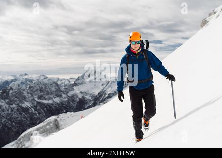 Porträt eines Bergsteigers mit Schutzhelm und Sonnenbrille, der hoch oben in den Bergen im Schnee steht Stockfoto