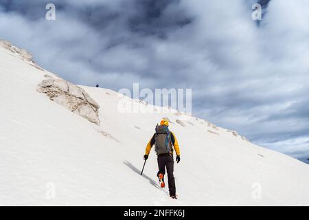 Rückblick auf einen unbekannten Bergsteiger mit einem Rucksack, der auf dem frischen Schnee entlang des Berges geht Stockfoto