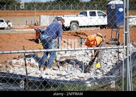 HICKORY, NC, USA – 14. FEBRUAR 2023: Zwei Bauarbeiter – einer mit Schaufel, einer mit Presslufthammer, hinter einem Kettengliederzaun. Stockfoto