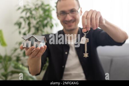 Immobilien- und Wohnungskonzept, glücklicher Seniorenmann zeigt auf ein Spielzeughaus in der Hand, Wohnungsleihe, Mietobjekt, Kopierraum. Stockfoto