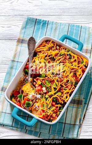 pinto Beans Speck Maisbrotsalat mit Tomaten, Paprika, Mais und Cheddar Käse in rechteckiger Schüssel auf weißem Holztisch mit Löffel vertikaler Ansicht von Stockfoto