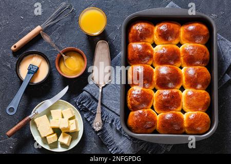 Hawaiianische süße Brötchen, portugiesisches süßes Brot, weiche und dehnbare Brötchen in Backform auf Betontisch mit Zutaten, horizontale Sicht von oben, fl Stockfoto