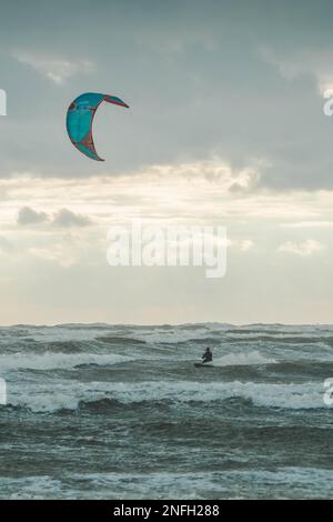 Ein vertikales Bild eines Kiteboarders auf stürmischem Meer an einem düsteren Tag Stockfoto