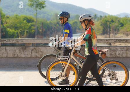 Asiatisches Fahrradpaar, das eine Pause vom Radfahren macht, macht eine Pause, geht spazieren und redet miteinander, um sich zu entspannen. Stockfoto