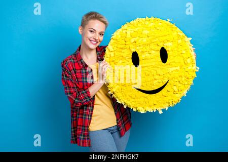 Foto eines hübschen netten Mädchens mit kurzen Haaren, einem roten Hemd, das ein großes lächelndes Emoji auf blauem Hintergrund hält Stockfoto