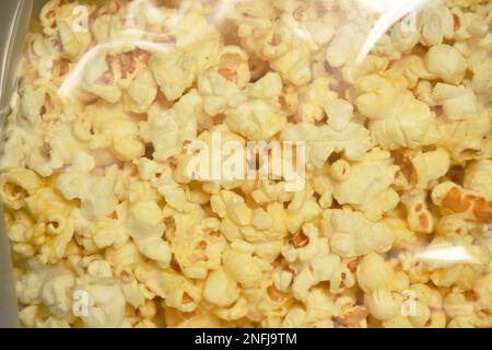 Salziges Popcorn in durchsichtiger Kunststoffverpackung auf weißem Hintergrund Stockfoto