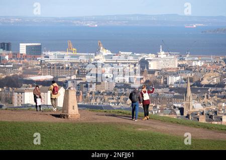 Edinburgh, Schottland, Großbritannien. 17. Februar 2023 Besucher auf dem Calton Hill, die sich gegen den kalten, stürmischen Wind gewandt haben. Blick über die Dächer der Stadt mit Blick nach Norden über die vierte Flussmündung in Richtung Fife. Kredit: Craig Brown/Alamy Live News Stockfoto