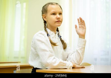 Eine Schülerin erhebt ihre Hand, bereit, die Fragen des Lehrers in einem hellen Klassenzimmer zu beantworten. Platz für Text. Das Konzept der Bildung, zurück zur Schule. Hochwertiges Foto Stockfoto