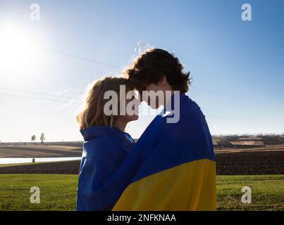 Junges Paar, männliches Mädchen, gegenüberliegend, mit ukrainischer Flagge eingewickelt. Unabhängigkeitstag. Konzept von Liebe und Patriotismus. Freiheit, Frieden Stockfoto