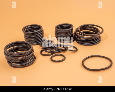 Hydraulische und pneumatische O-Ringe in Schwarz in verschiedenen Größen auf orangefarbenem Hintergrund. Gummidichtungen für Rohrleitungen. Speicherplatz kopieren. Stockfoto