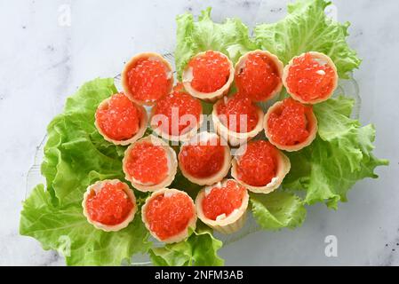 Törtchen mit Butter und rotem Kaviar. Teller mit Kaviar-Vorspeise, dekoriert mit Salatblättern auf hellem Hintergrund Stockfoto