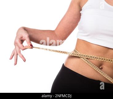 Eine Frau in einem weißen Crop-Top und einer schwarzen Yoga-Hose, die ein Maßband um ihre Taille wickelt, um Gewichtsverlust zu zeigen Stockfoto