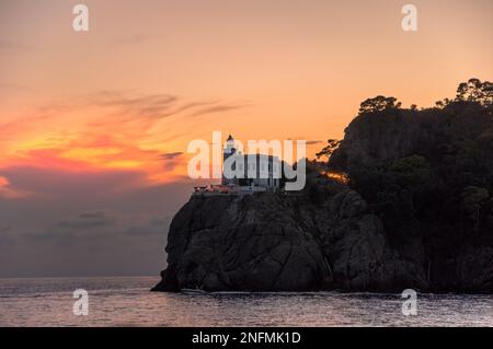 Ein herrlicher Sonnenuntergang am historischen Leuchtturm Faro di Portofino in Portofino, Ligurien, Italien. Ein Foto vom Meer unten mit dem felsigen Berg Stockfoto