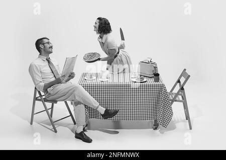 Schwarzweiß-Porträt eines Paares, das am Tisch sitzt und frühstückt. Filmneuaufbau. Die Frau versteckt das Messer hinter dem Rücken Stockfoto