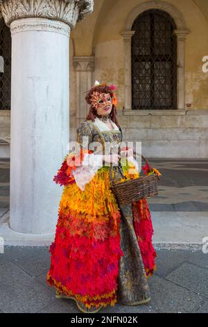 Karnevalsgast gekleidet in herrlichem Kostümkleid und Maske Venedig Karneval 2023 am Markusplatz, Venedig, Italien im Februar - Herbstlaub Konzept Stockfoto