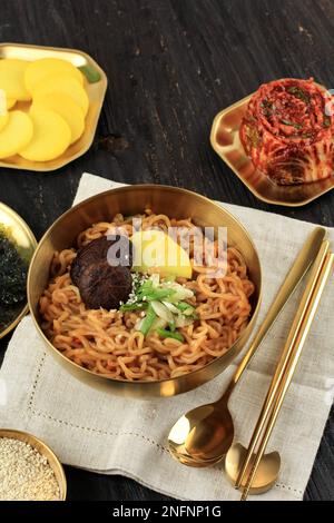 Scharfe gebratene koreanische Instant-Nudeln aus Ramyeon mit Danmuji, Pilz, Sesamsamen, Kimchi und grünen Zwiebeln. Auf Einem Holztisch Stockfoto