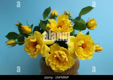 Gelbe Rosen mit zarten Blütenblättern und grünen Blättern auf blauem Hintergrund, Strauß gelber Rosen mit Knospen in der Vase, Frühlingsblumen, Stockfoto